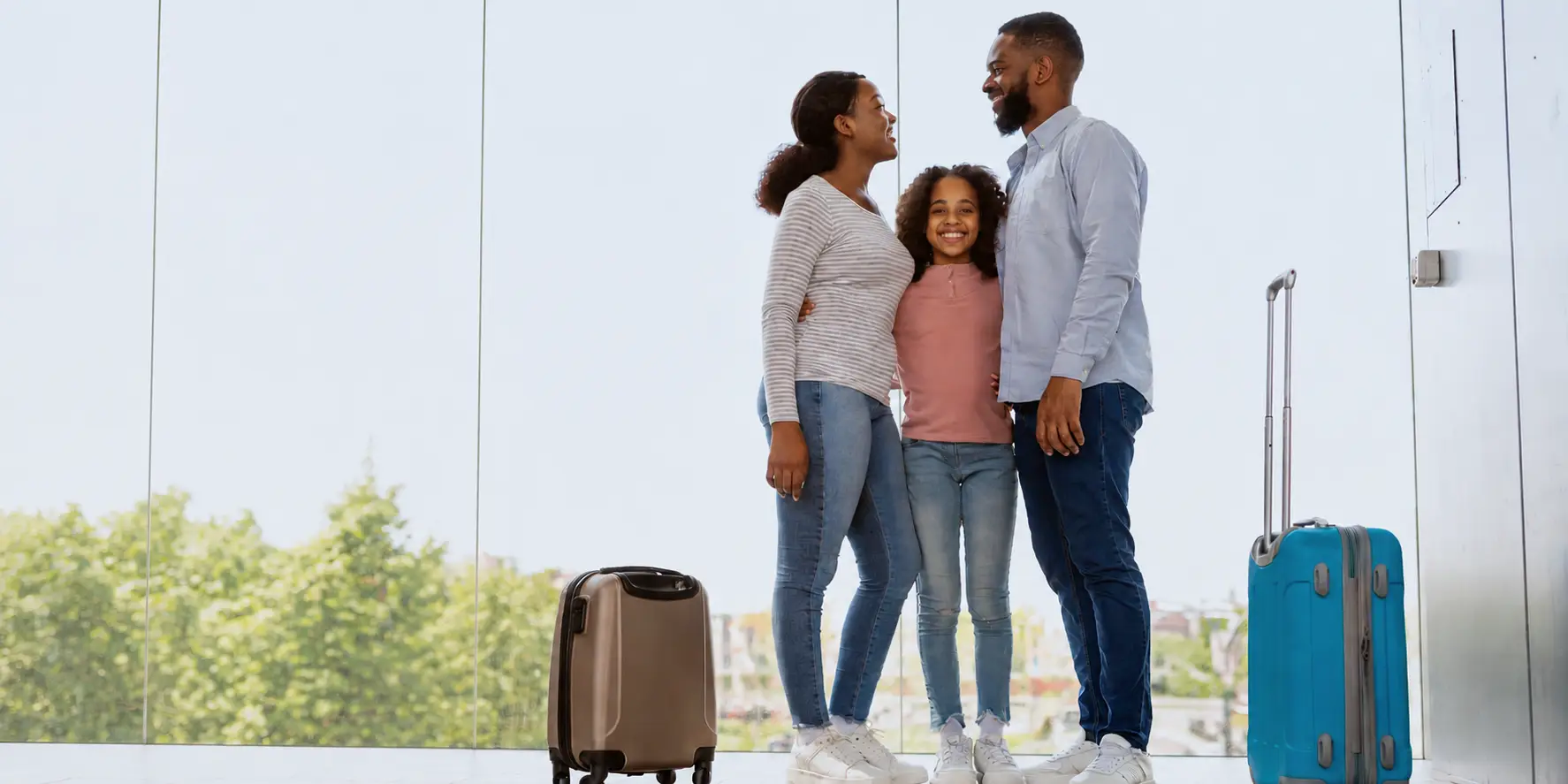 Family standing beside brown and turquoise rolling suitcases in a bright airport terminal