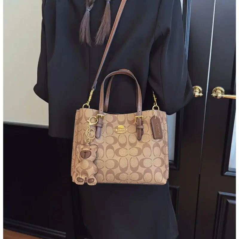 Person in dark clothing holding a beige printed tote bag with brown handles