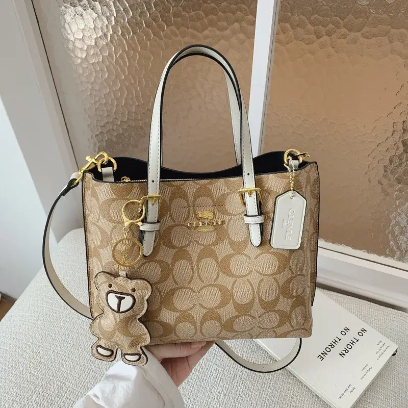 Tan printed tote bag with contrasting light and dark carry handles displayed against a beige background
