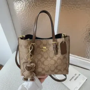 Tan printed tote bag with dark handles and a hanging tag displayed on a sofa