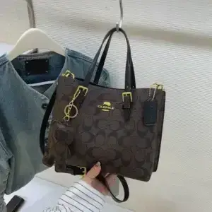 Brown printed tote bag with dark carry handles hanging beside green clothing