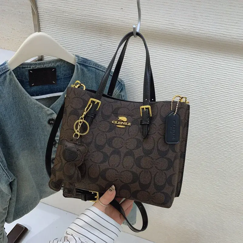 Brown printed tote bag with dark carry handles hanging beside green clothing