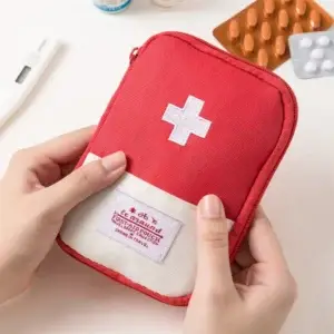 Hands holding a red zippered first aid pouch with a white cross
